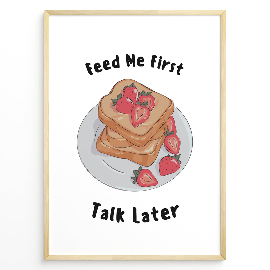 Funny kitchen poster with a plate of toast and strawberries, and the text “Feed Me First Talk Later,” framed in black on a white background.