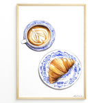 Indlæs billede til gallerivisning Art print of a cappuccino and croissant on blue patterned plates — French café-style kitchen wall décor.
