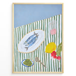 Indlæs billede til gallerivisning Mediterranean still life poster with fish on a white plate, lemon, radishes, olives, and a pink drink on a green and white striped tablecloth, framed as kitchen wall art.
