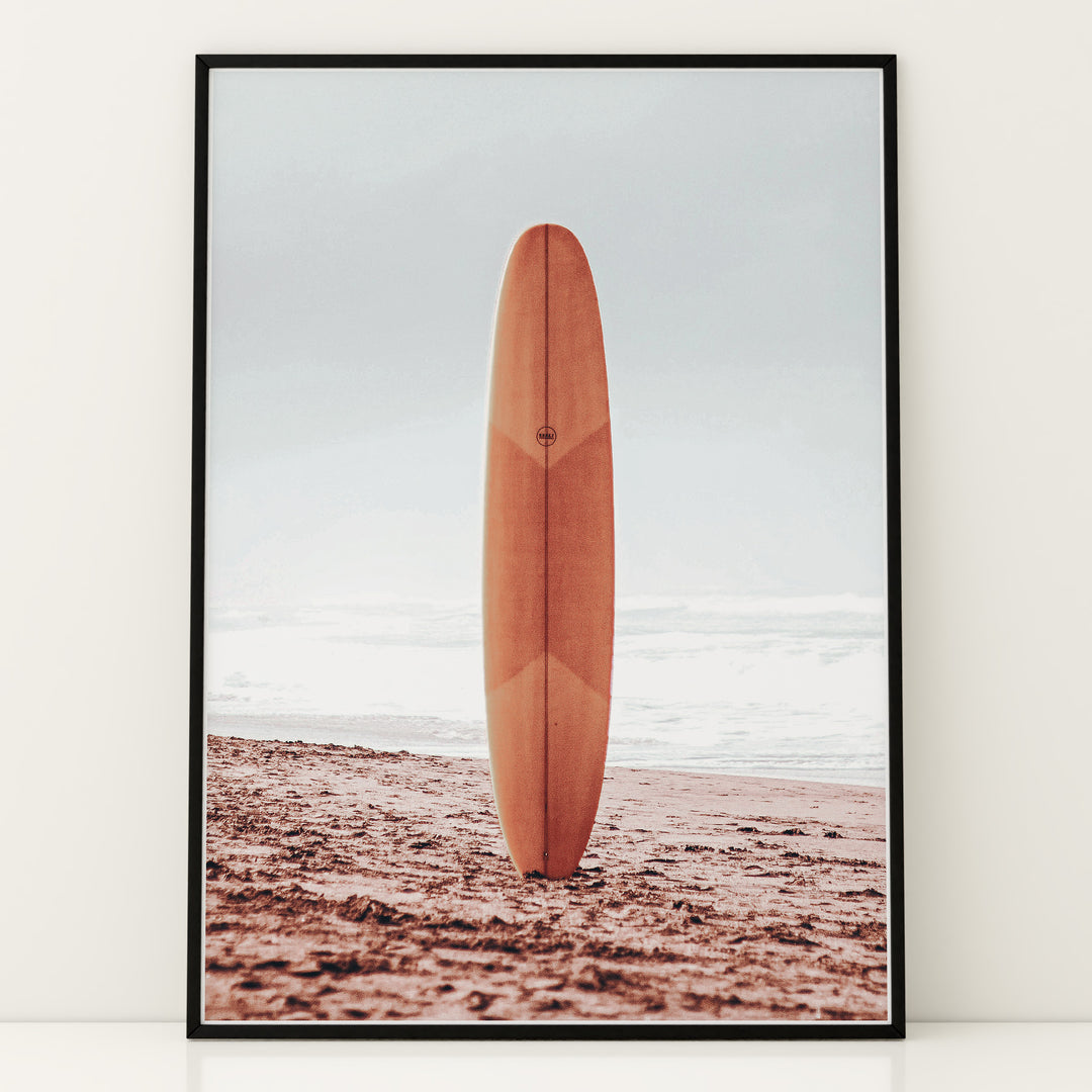 Plakat med surfbræt på stranden | Sommer og Strand Plakater | Denne plakat viser et surfbræt stående oprejst på en rolig sandstrand med havet i baggrunden. Perfekt til strand- og surfentusiaster.