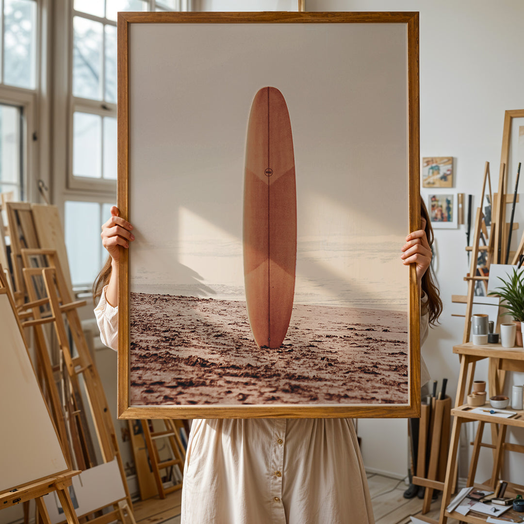 Plakat med surfbræt på stranden | Sommer og Strand Plakater | Denne plakat viser et surfbræt stående oprejst på en rolig sandstrand med havet i baggrunden. Perfekt til strand- og surfentusiaster.