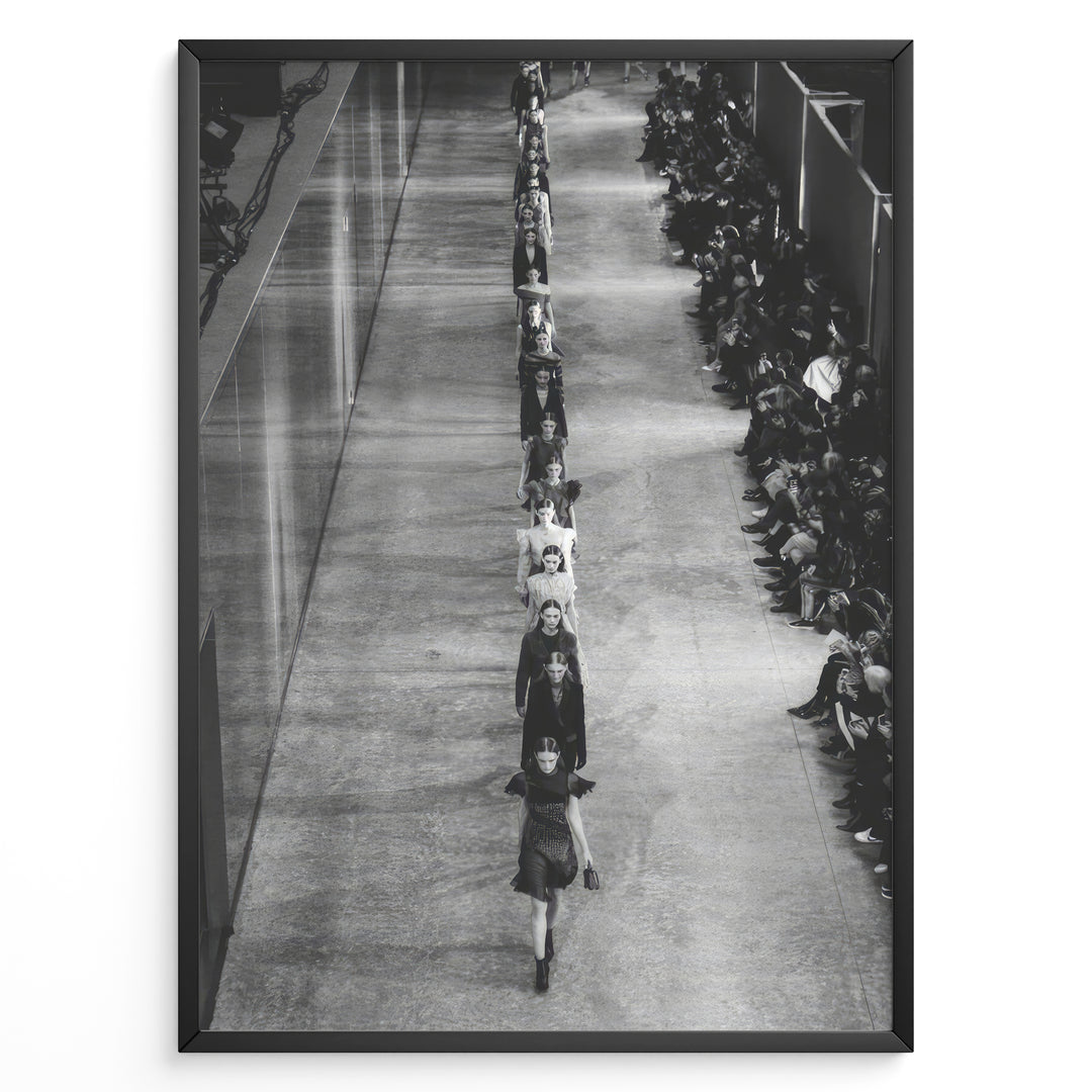 Fashion Plakat | Black & White Fashion Runway – Editorial Wall Art Print Plakaty.dk | Black and white photograph of runway models walking in a single-file line during a fashion show, with seated spectators on one side of the runway.