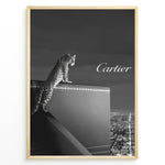 Indlæs billede til gallerivisning Fashion Plakat | Cartier Panther Over the City: Iconic Elegance in Monochrome Plakaty.dk | Black and white image of a panther perched on a Cartier box overlooking a city skyline at night, with the Cartier logo in the sky.
