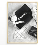 Indlæs billede til gallerivisning Fashion Plakat | Chanel Gift Box &amp; Handbag Flatlay Wall Art Plakaty.dk | Black and white flatlay of a Chanel gift box with ribbon, camellia flowers, and a quilted Chanel handbag on a soft surface.
