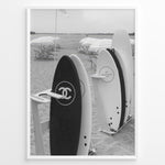 Indlæs billede til gallerivisning Fashion Plakat | Chanel Surfboards on the Beach – Luxury Meets Coastal Lifestyle in Black and White Plakaty.dk | Black and white photo of Chanel and J12 Yacht Club surfboards on a sandy beach with umbrellas and lounge chairs in the background
