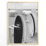 Indlæs billede til gallerivisning Fashion Plakat | Chanel Surfboards on the Beach – Luxury Meets Coastal Lifestyle in Black and White Plakaty.dk | Black and white photo of Chanel and J12 Yacht Club surfboards on a sandy beach with umbrellas and lounge chairs in the background
