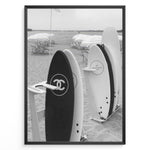 Indlæs billede til gallerivisning Fashion Plakat | Chanel Surfboards on the Beach – Luxury Meets Coastal Lifestyle in Black and White Plakaty.dk | Black and white photo of Chanel and J12 Yacht Club surfboards on a sandy beach with umbrellas and lounge chairs in the background
