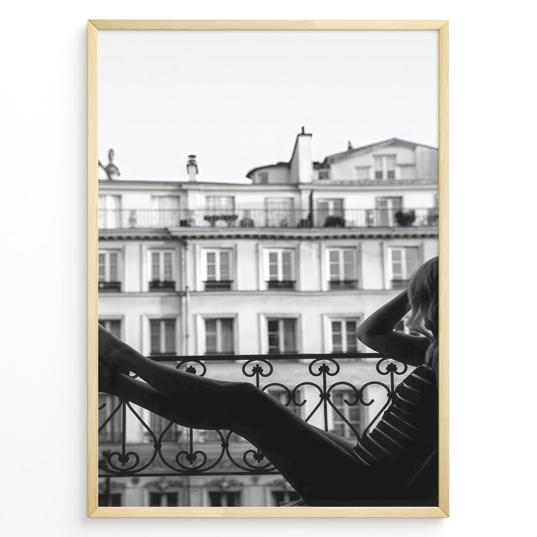 Fashion Plakat | Elegant Woman Relaxing on Parisian Balcony – Black and White Photography Plakaty.dk | Black and white photo of a woman relaxing on a Parisian balcony with classic building architecture in the background