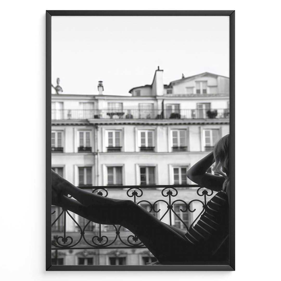 Fashion Plakat | Elegant Woman Relaxing on Parisian Balcony – Black and White Photography Plakaty.dk | Black and white photo of a woman relaxing on a Parisian balcony with classic building architecture in the background
