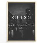 Indlæs billede til gallerivisning Fashion Plakat | Gucci Cityscape Black &amp; White Fashion Poster Plakaty.dk | Black and white poster with the Gucci logo over a night cityscape featuring tall buildings and water reflections.
