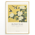 Indlæs billede til gallerivisning Japanske plakater | Japanese woodblock print of white trumpet lilies with green leaves and two sparrows flying against a yellow background, based on Hokusai’s  floral artwork.
