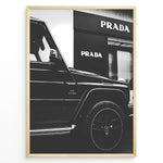 Indlæs billede til gallerivisning Fashion Plakat | Mercedes-Benz G-Wagon and Prada Store Black and White Art Print Plakaty.dk | A framed, black and white photograph showing the side profile of a Mercedes-Benz G-Wagon AMG parked in front of a Prada store. The car&#39;s V8 BITURBO badge is visible, and the Prada logo is prominent on the building&#39;s facade.
