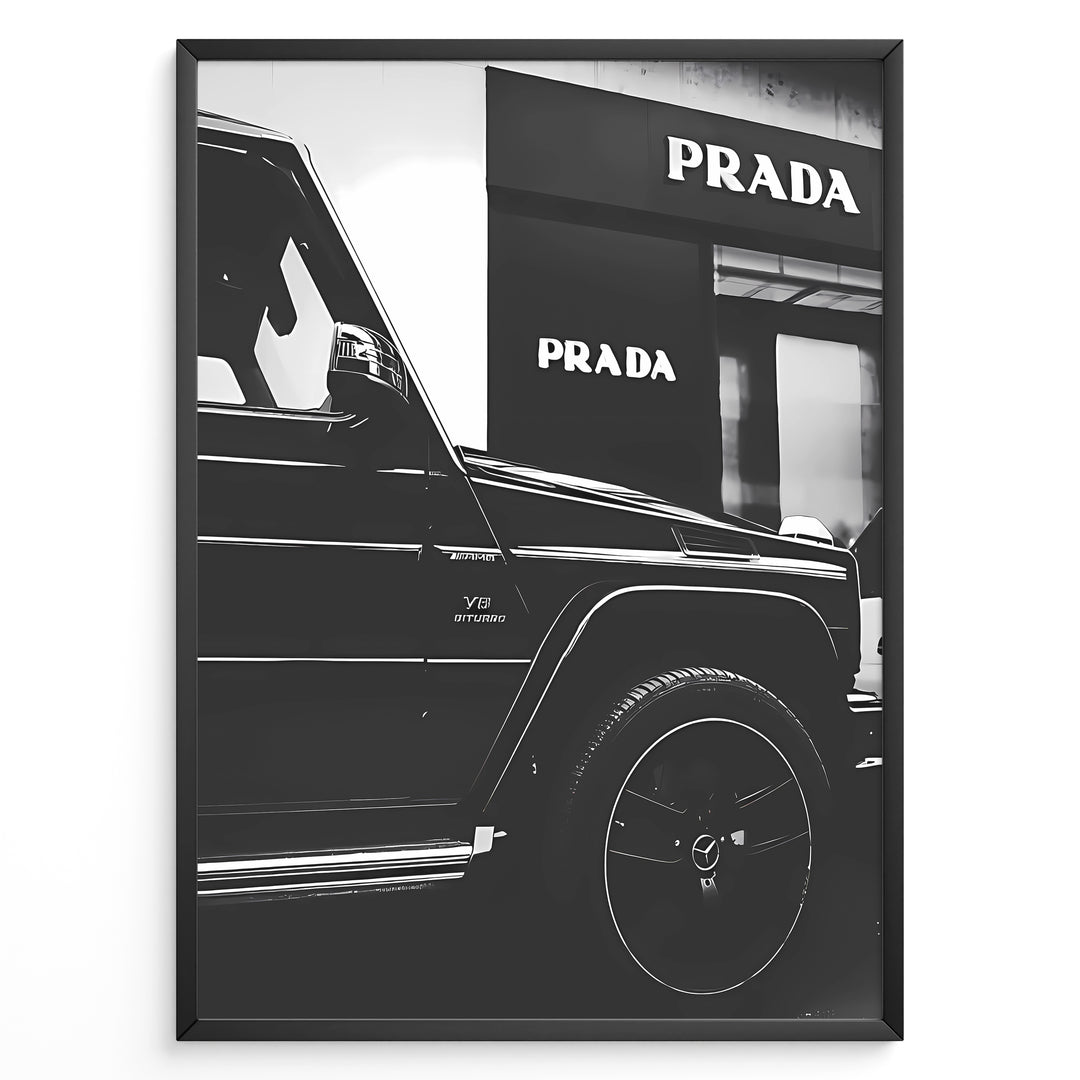 Fashion Plakat | Mercedes-Benz G-Wagon and Prada Store Black and White Art Print Plakaty.dk | A framed, black and white photograph showing the side profile of a Mercedes-Benz G-Wagon AMG parked in front of a Prada store. The car's V8 BITURBO badge is visible, and the Prada logo is prominent on the building's facade.