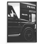 Indlæs billede til gallerivisning Fashion Plakat | Mercedes-Benz G-Wagon and Prada Store Black and White Art Print Plakaty.dk | A framed, black and white photograph showing the side profile of a Mercedes-Benz G-Wagon AMG parked in front of a Prada store. The car&#39;s V8 BITURBO badge is visible, and the Prada logo is prominent on the building&#39;s facade.
